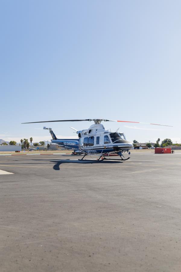 A helicopter blue and white in color parked on the flight line of an airport under clear blue skies.